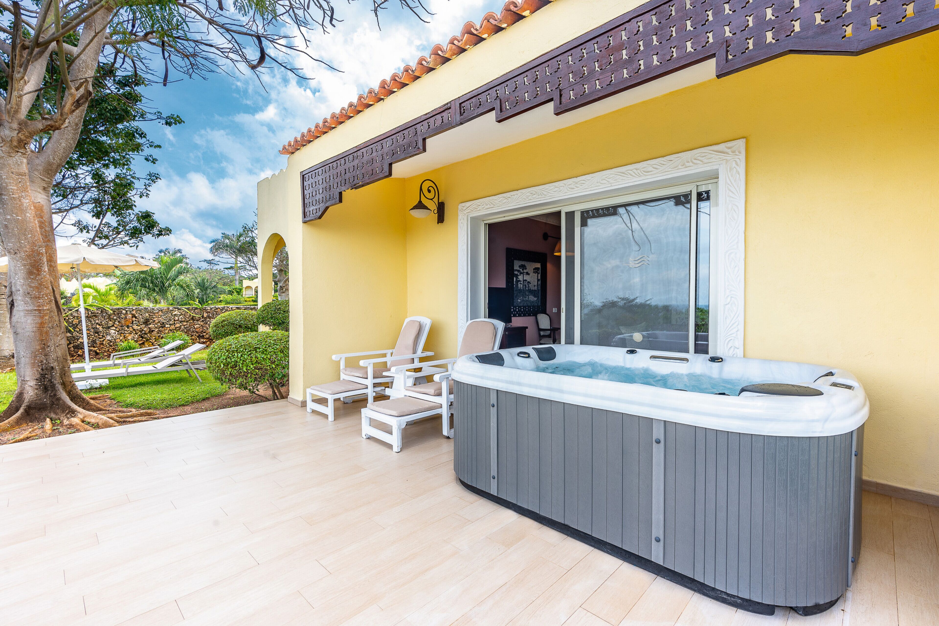 A hot tub in a sunlit outdoor area with lounge chairs and a view of a garden.