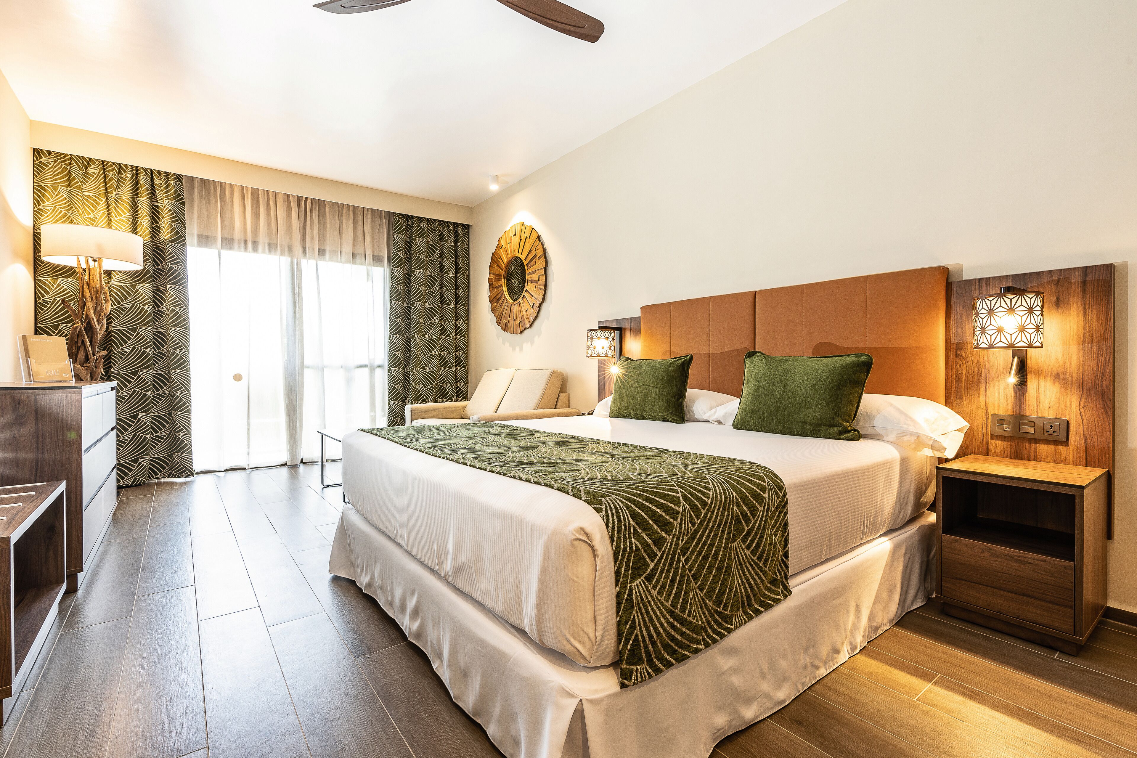 Habitación de hotel con una cama grande, un escritorio, una silla, una mesita de noche y una lámpara de pared.