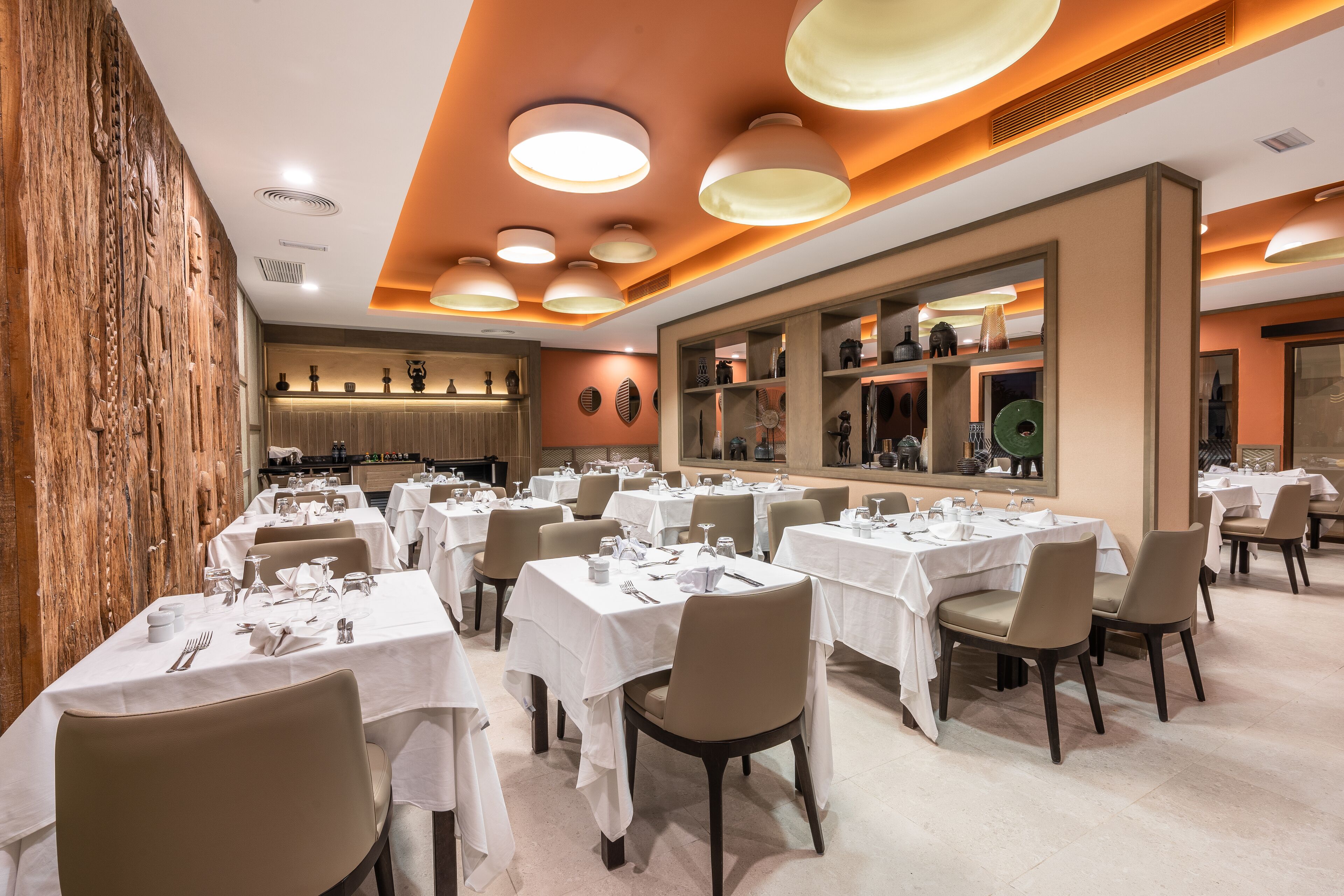 Un restaurant doté de nombreuses tables dressées pour le service, avec un intérieur moderne agrémenté d’un mur en bois et d’un grand miroir.