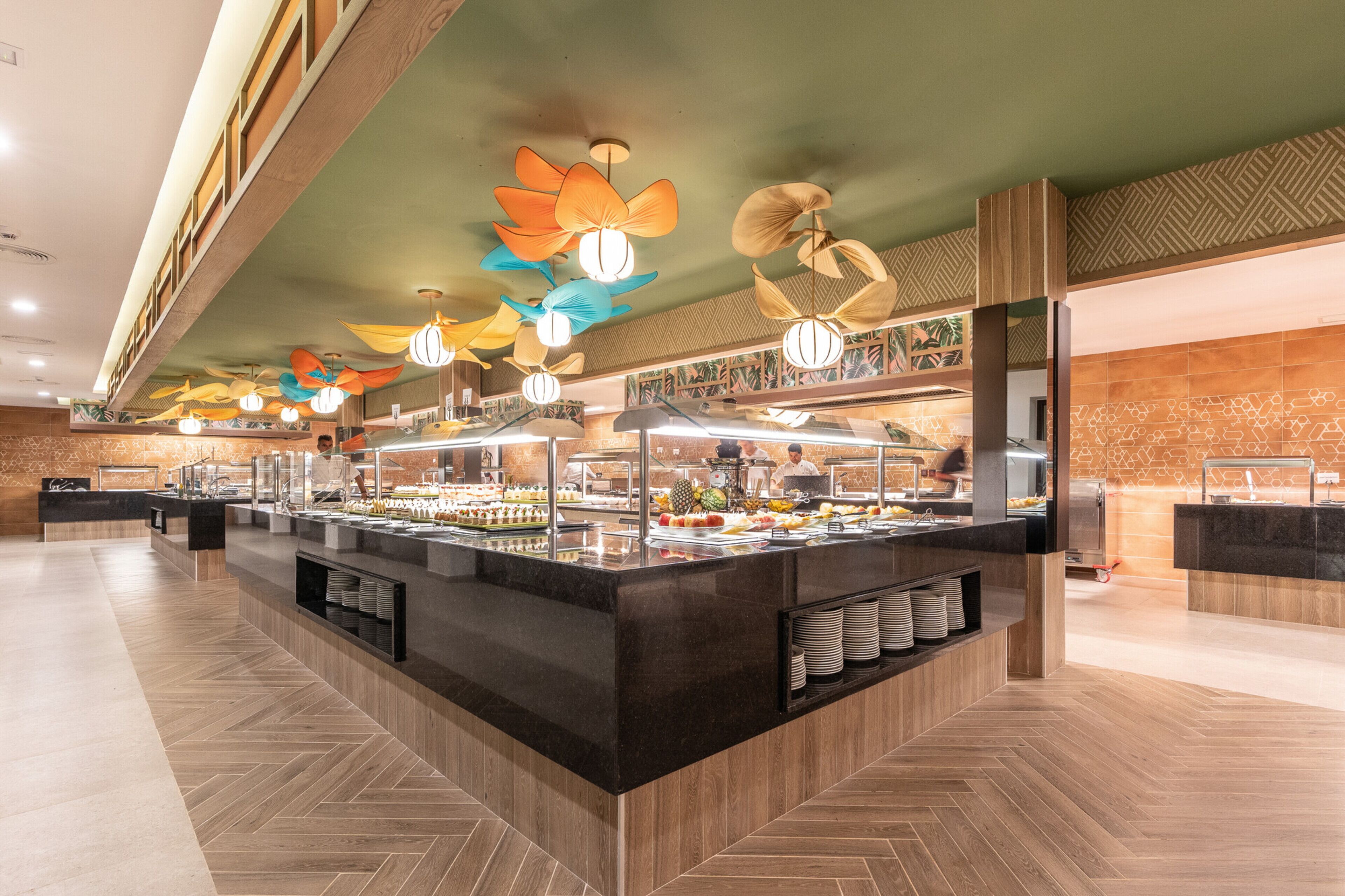 A buffet area with multiple food stations, a herringbone floor pattern, and decorative ceiling lights.