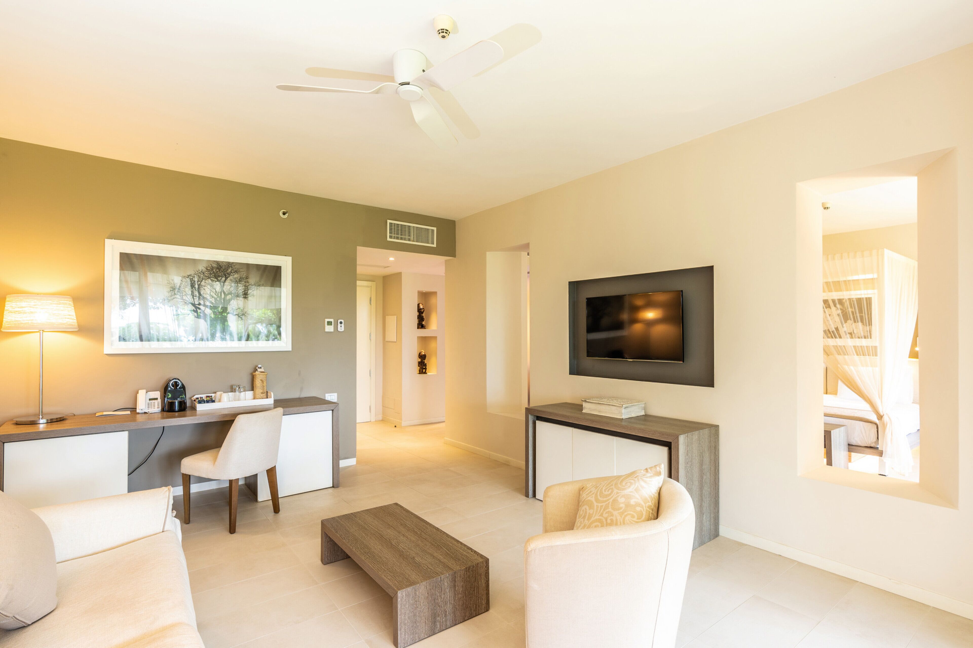 A modern living room with a sofa, coffee table, TV, and a desk area with a lamp and a framed picture.