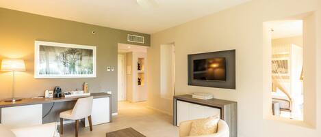 A modern living room with a sofa, coffee table, TV, and a desk area with a lamp and a framed picture.
