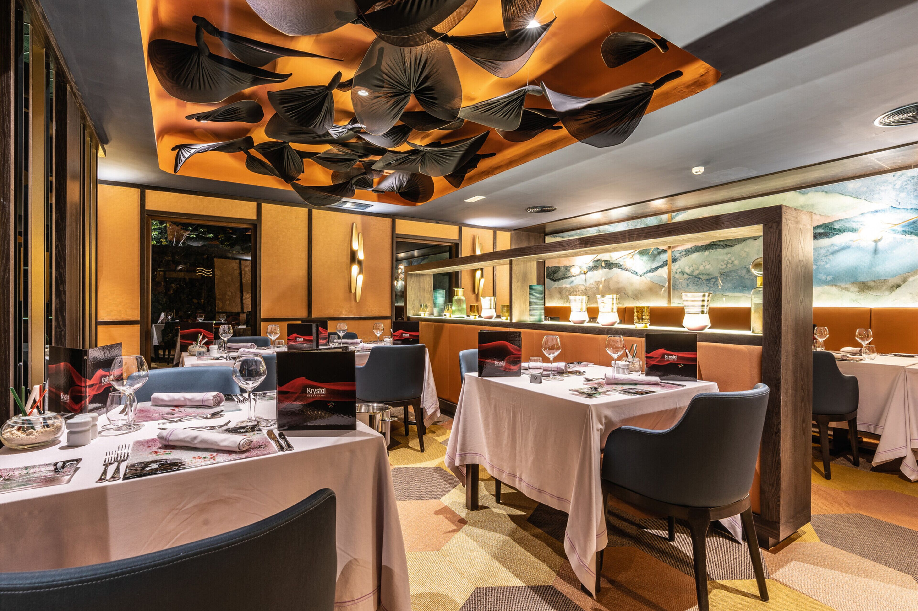 Un restaurante con mesas dispuestas para comer, una zona de bar y un techo decorativo.