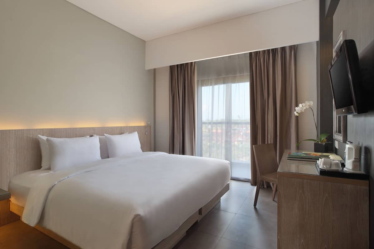 Une chambre d’hôtel avec un grand lit, un bureau doté d’un téléviseur à écran plat, une chaise et une fenêtre avec des rideaux.
