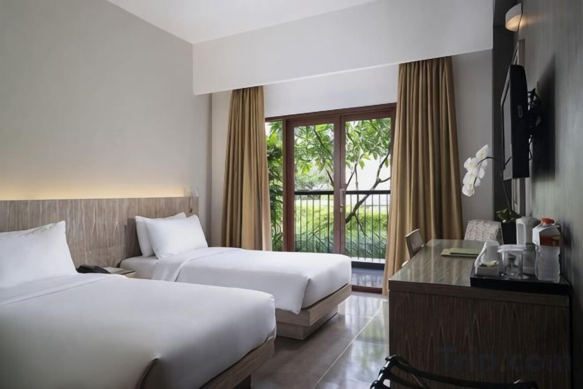Une chambre d’hôtel avec deux lits, un bureau avec une chaise, une fenêtre avec des rideaux et une vue sur la verdure.