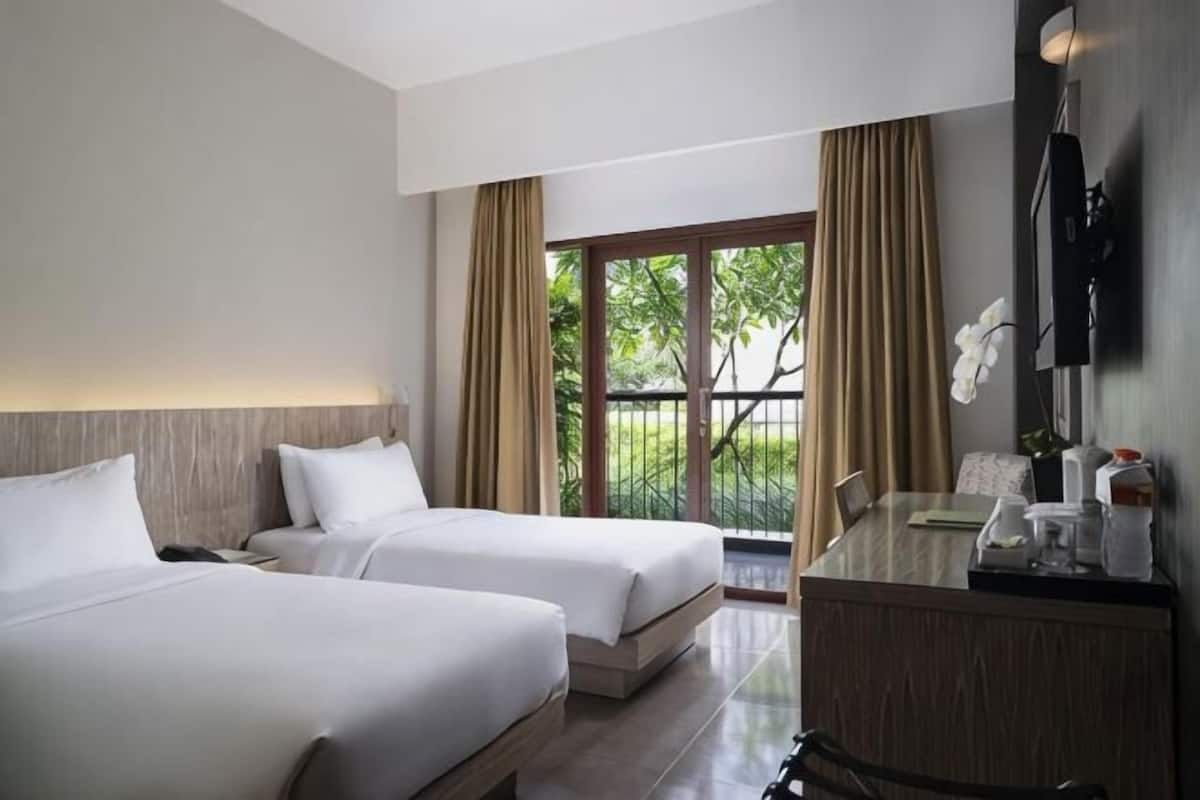Une chambre d’hôtel avec deux lits, un bureau, une chaise, une télévision et une fenêtre avec des rideaux.