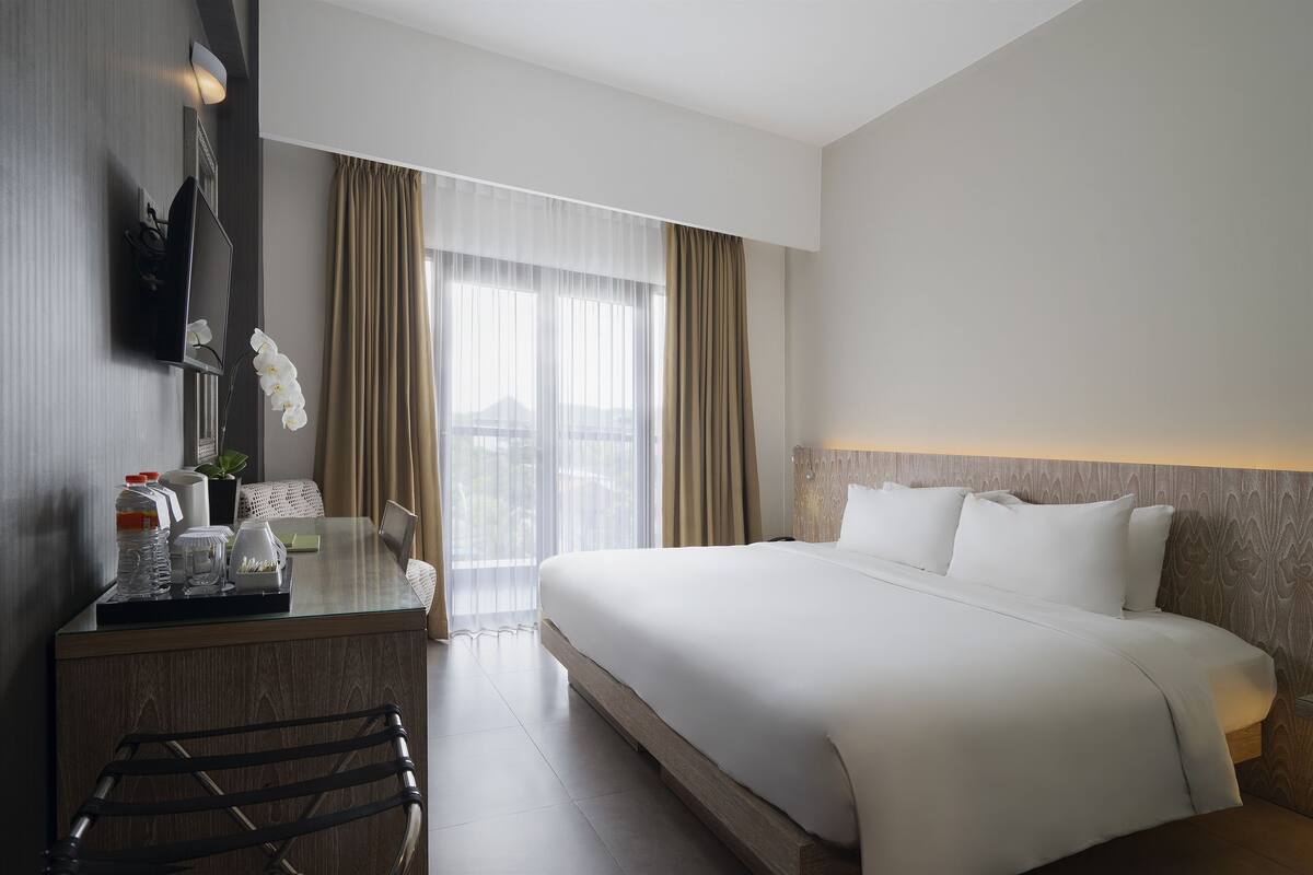 Une chambre d’hôtel avec un grand lit, un bureau équipé d’un ordinateur, une chaise et une vue sur la ville par la fenêtre.