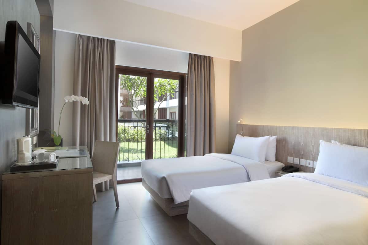 Une chambre d’hôtel avec deux lits, un bureau avec une télévision, une chaise et une vue sur l’extérieur.
