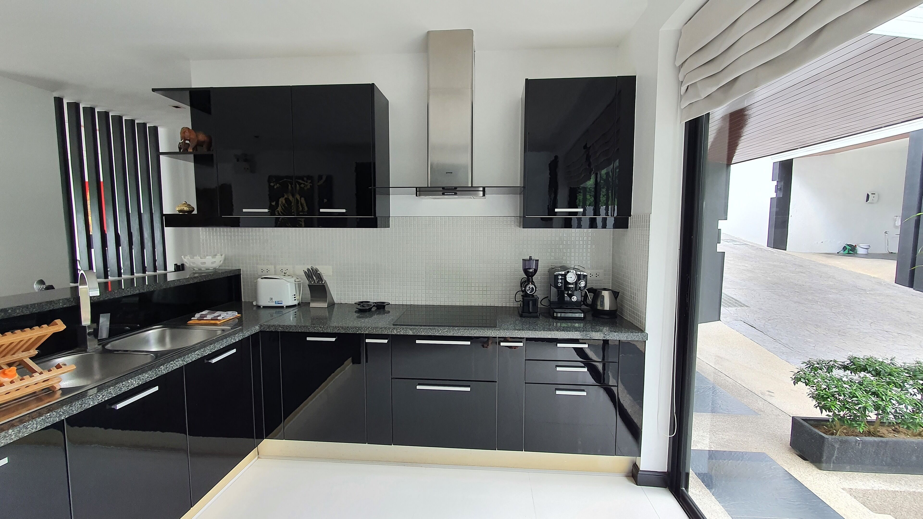 A modern kitchen with black cabinets, a stainless steel sink, and a coffee machine.