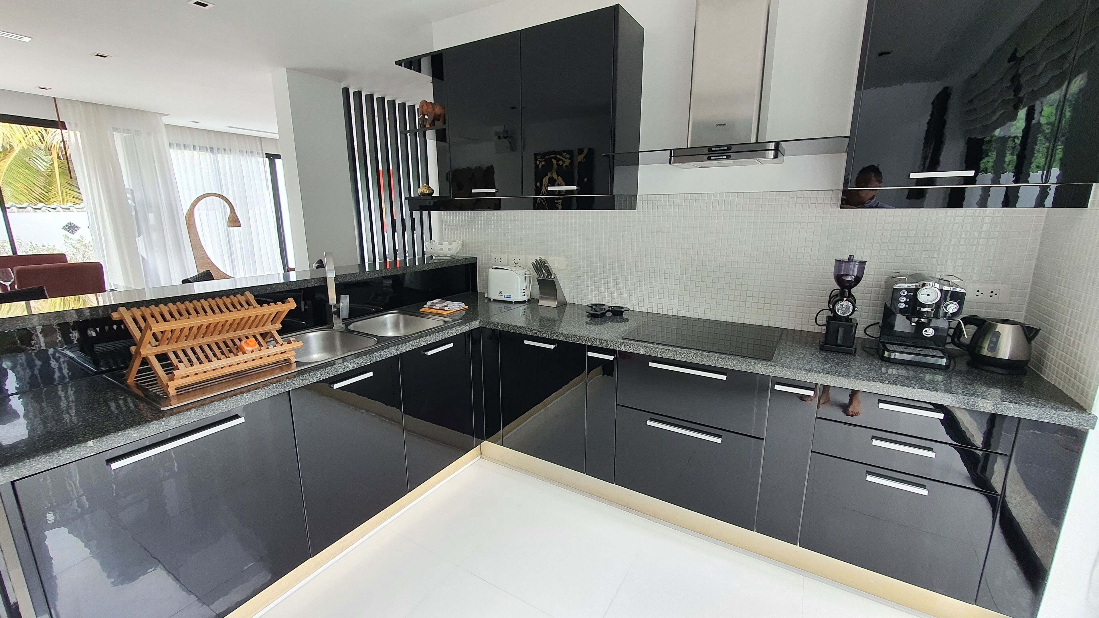 Una cocina moderna con armarios negros, encimera de granito, horno integrado y máquina de café.