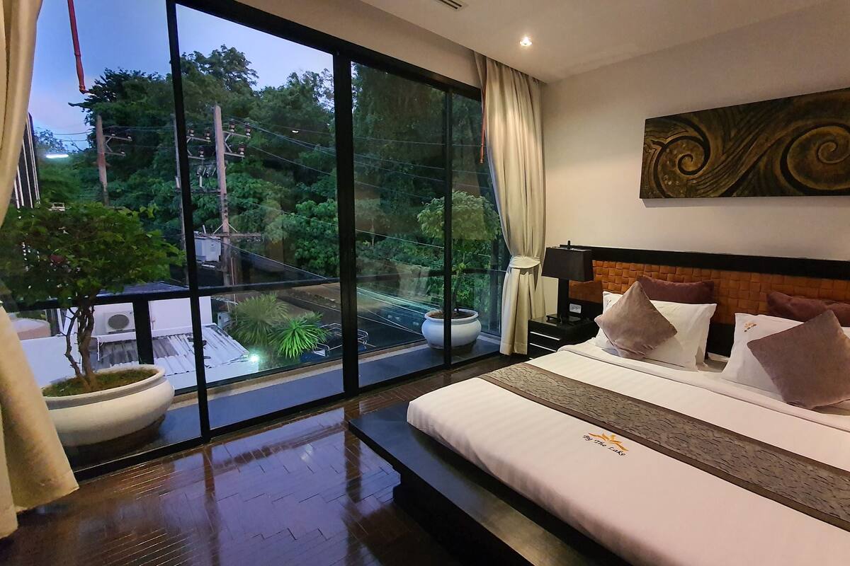 Una habitación de hotel moderna con un ventanal grande, una cama con ropa blanca y un adorno en la pared.