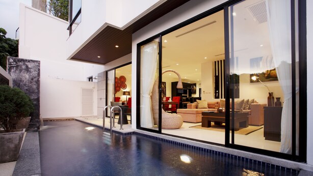 Una casa moderna con piscina, puertas de cristal amplias que dan a una sala de estar amoblada.