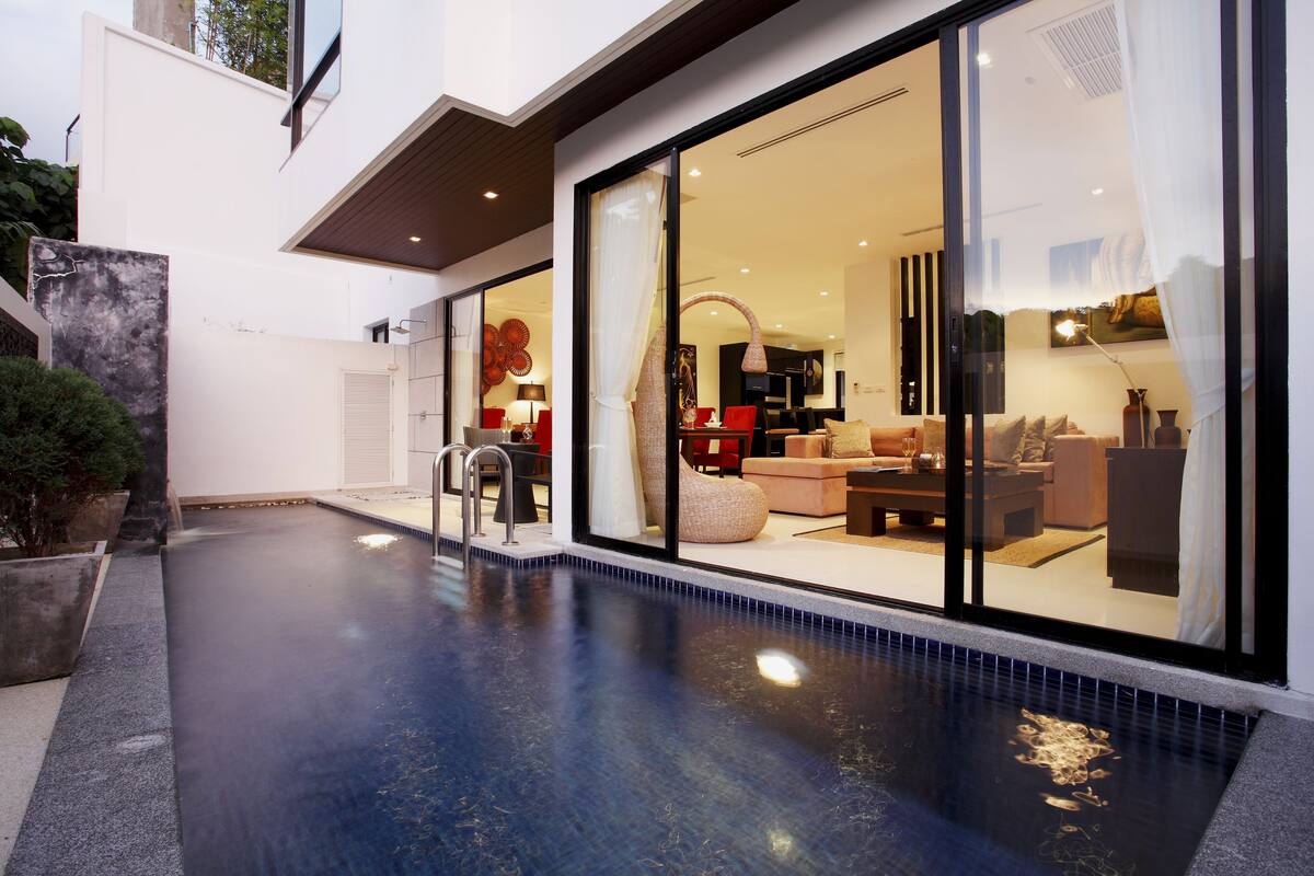 Una casa moderna con piscina, puertas de cristal amplias que dan a una sala de estar amoblada.