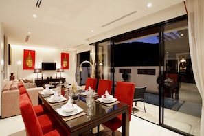 A modern dining area with a long table set for six, red upholstered chairs, and a large window offering a view of the night sky.