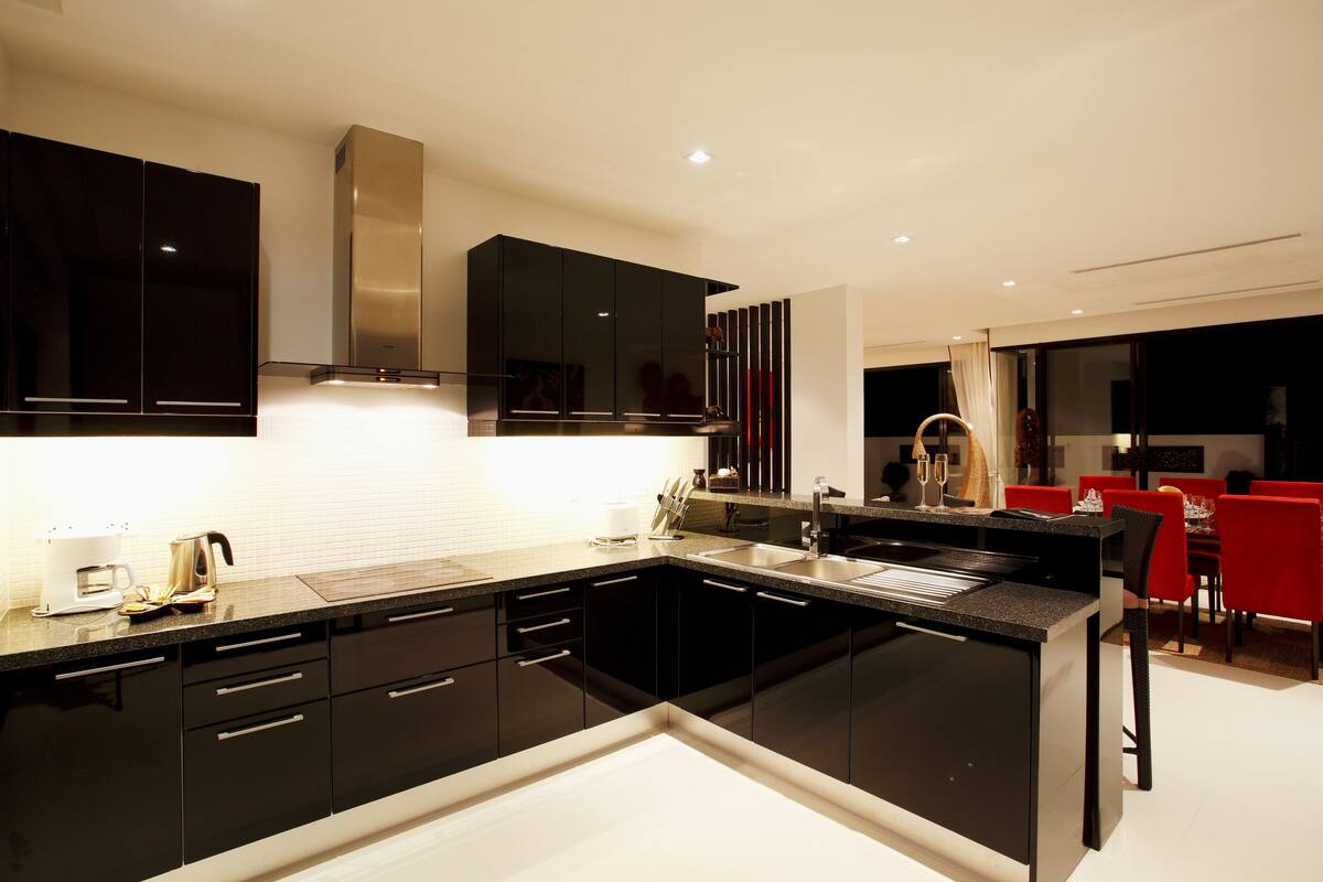 Una cocina moderna con gabinetes negros, una campana extractora de acero inoxidable y un comedor con sillas rojas.