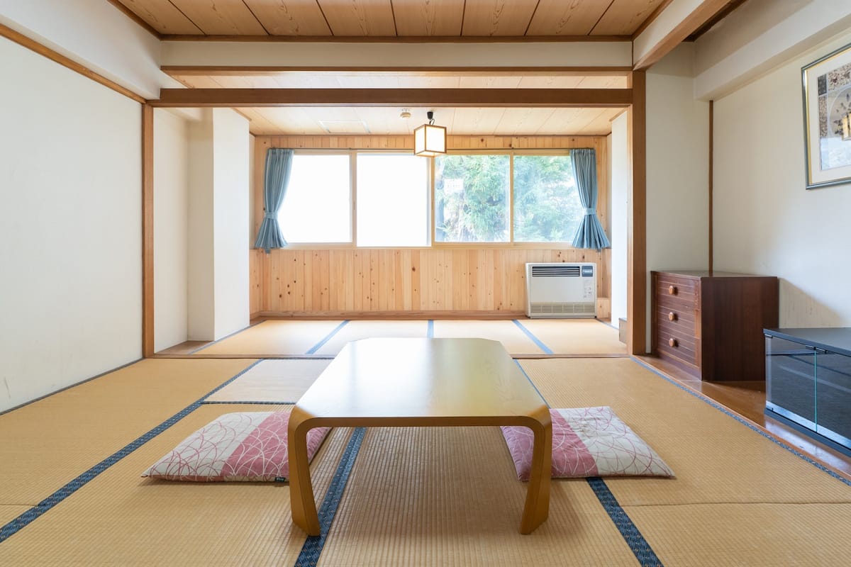A tatami mat room with a wooden table, a heater, and a window with curtains.