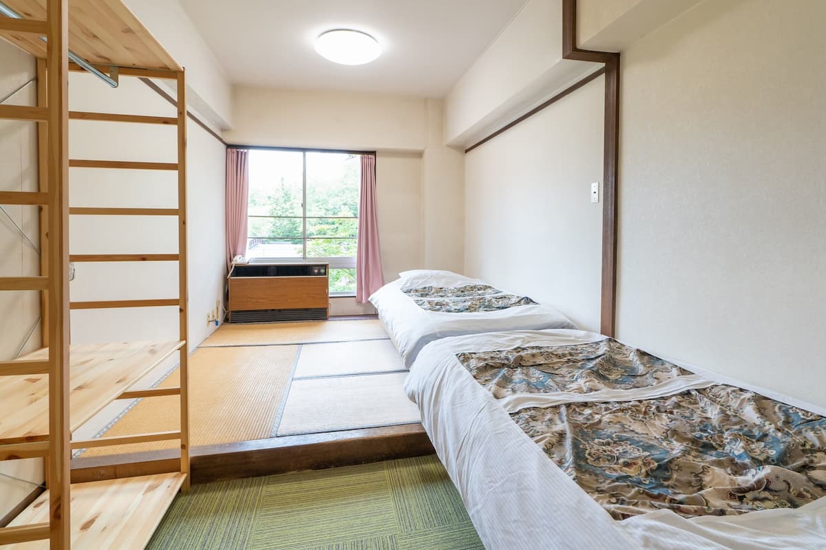 A room with a bed, a wooden ladder, a window with curtains, and a small table.