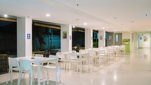 A spacious indoor dining area with white tables and chairs, large windows, and a clean, modern design. - POP! Hotel Kuta Beach Bali (Kuta)