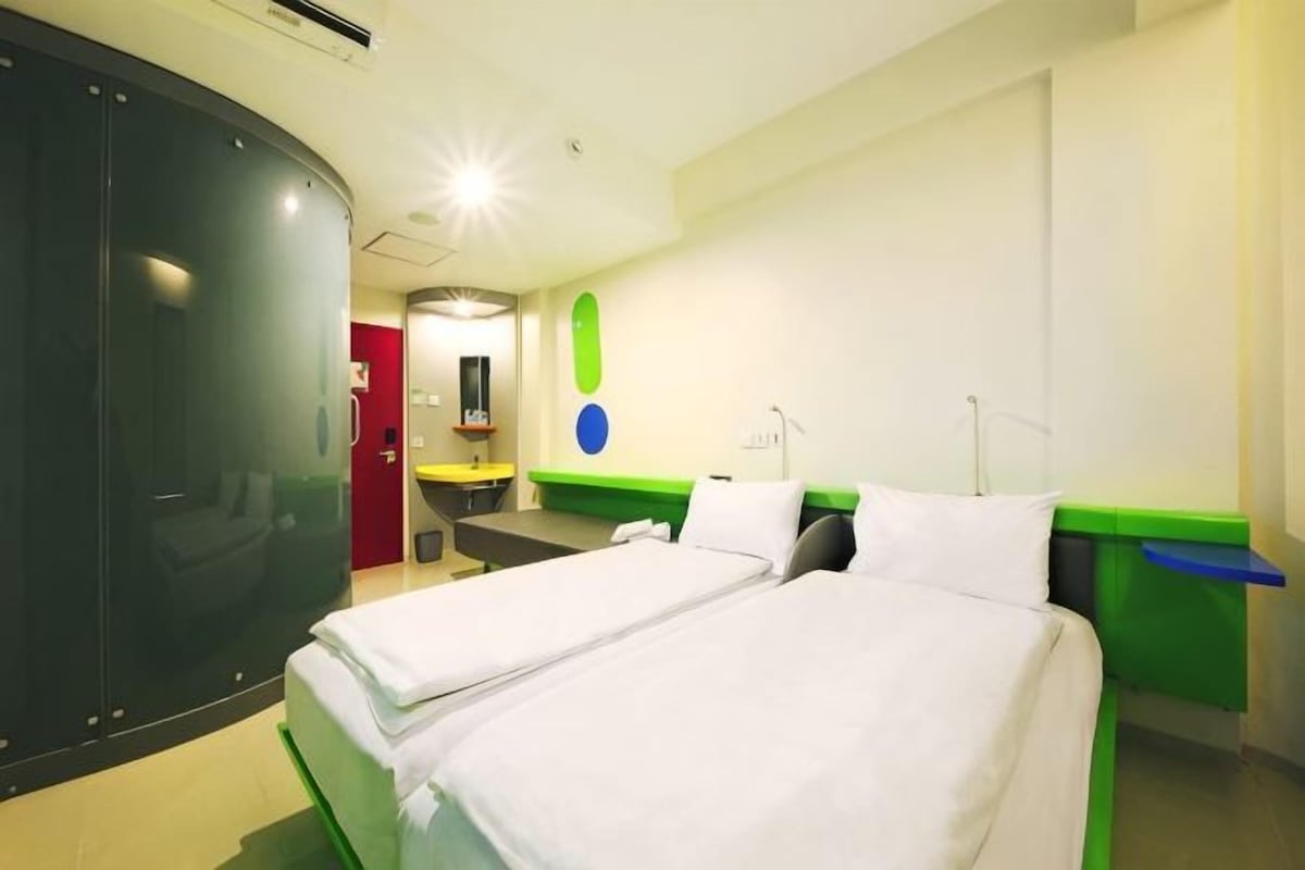 A hotel room with a bed, a desk, a chair, a mirror, and a wardrobe.