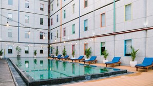 A modern indoor pool area with multiple lounge chairs and potted plants. - POP! Hotel Kuta Beach Bali (Kuta)