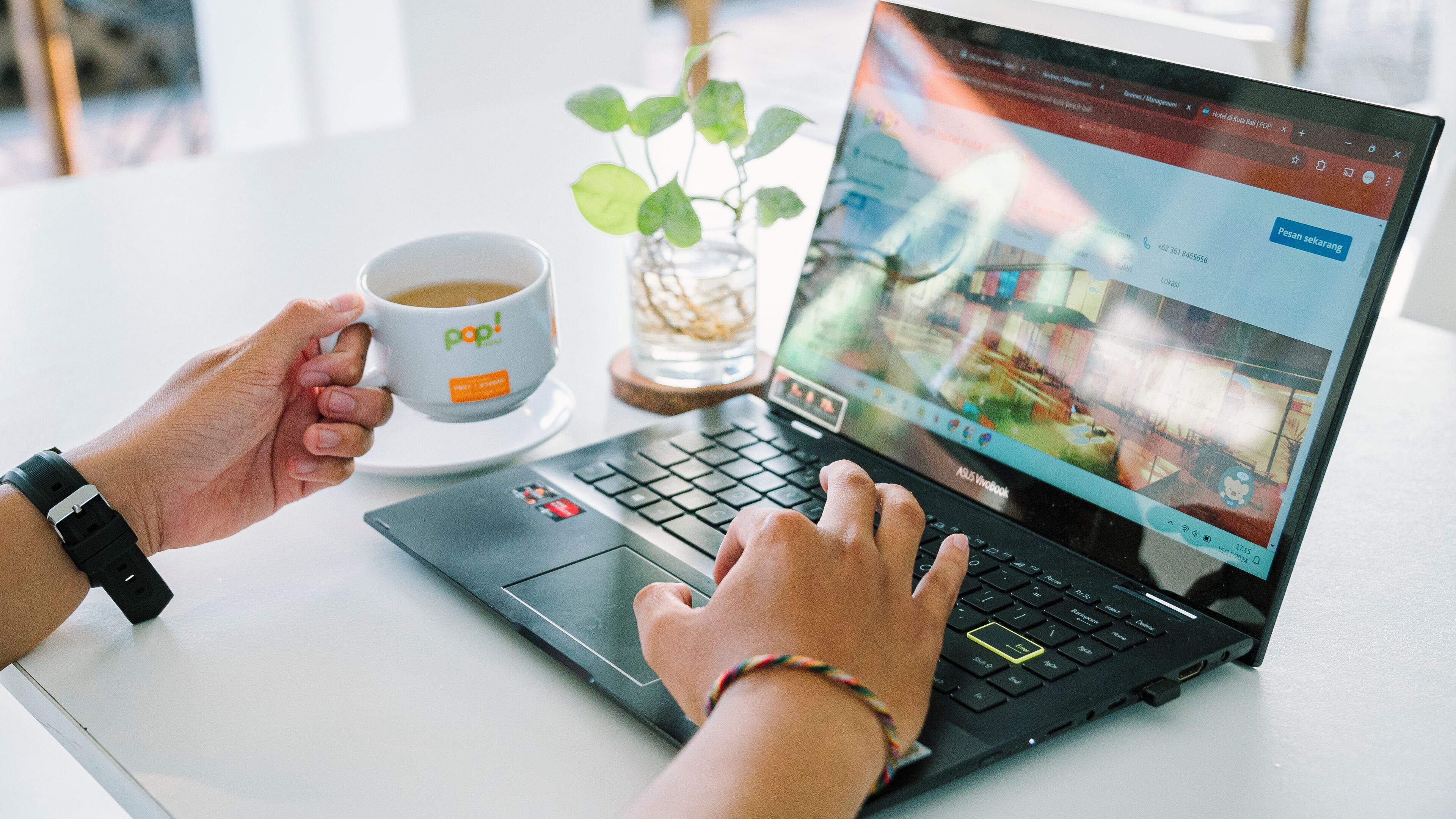 Een laptop op een tafel, met een kop koffie en een plant ernaast.
