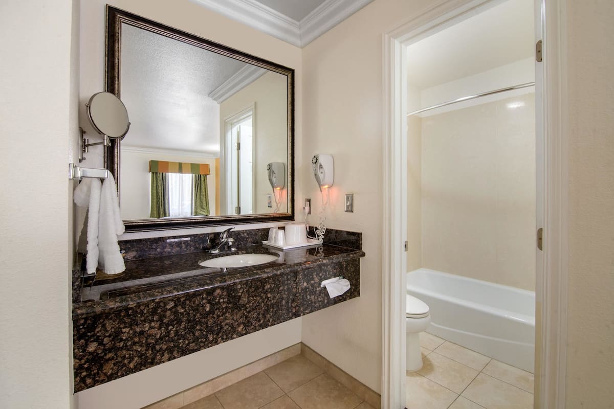 A bathroom with a granite countertop sink, a large mirror, a towel rack, a toilet, and a bathtub.