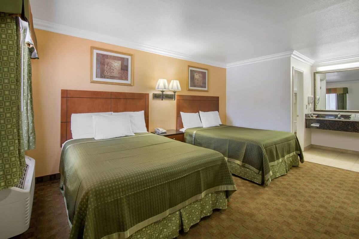 A hotel room with two beds, a bathroom with a mirror, and a wall with two framed pictures.