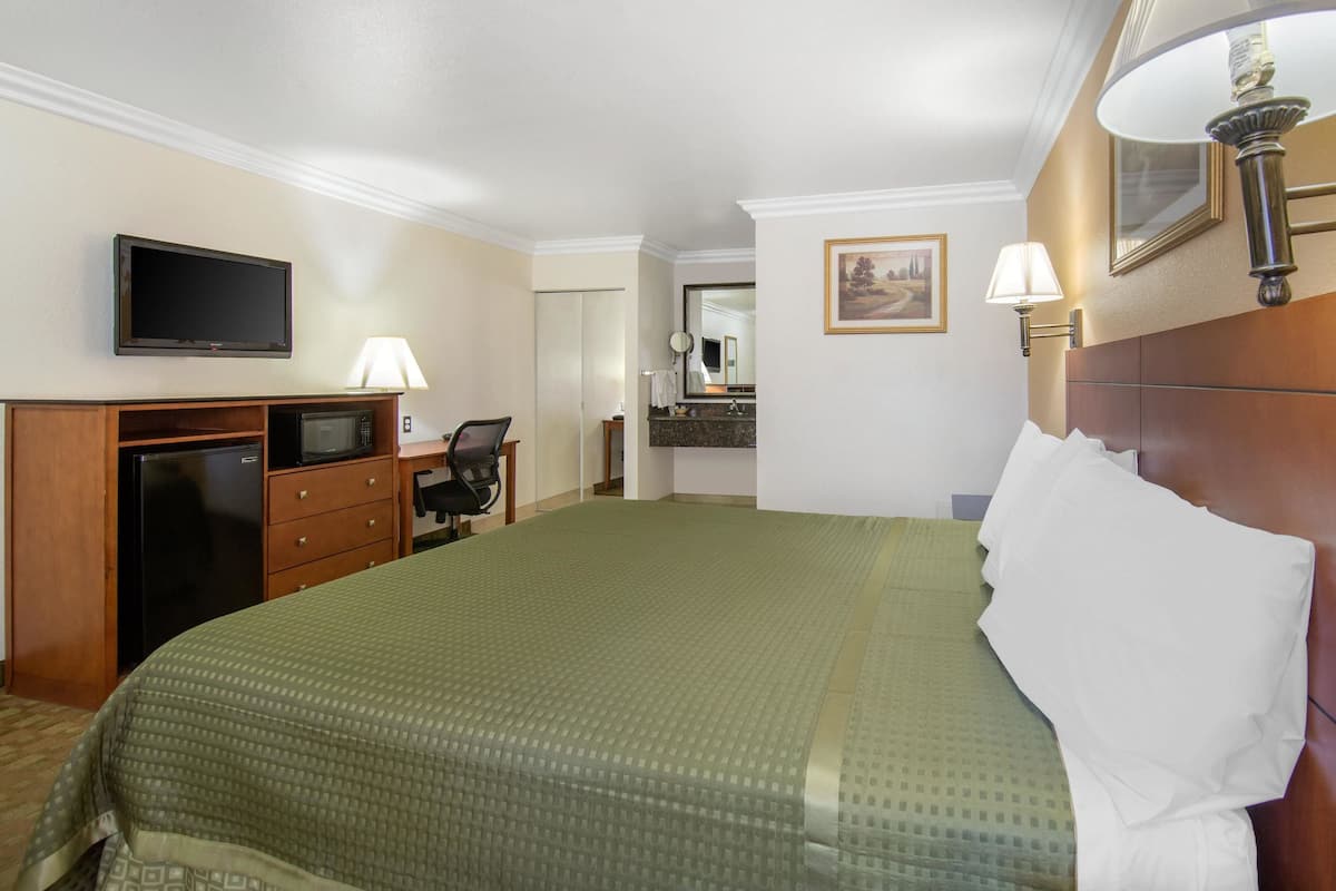 A hotel room with a bed, a desk with a computer, a television, and a bathroom visible through an open door.