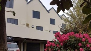 A modern two-story building with a garage, surrounded by lush greenery and flowering plants.