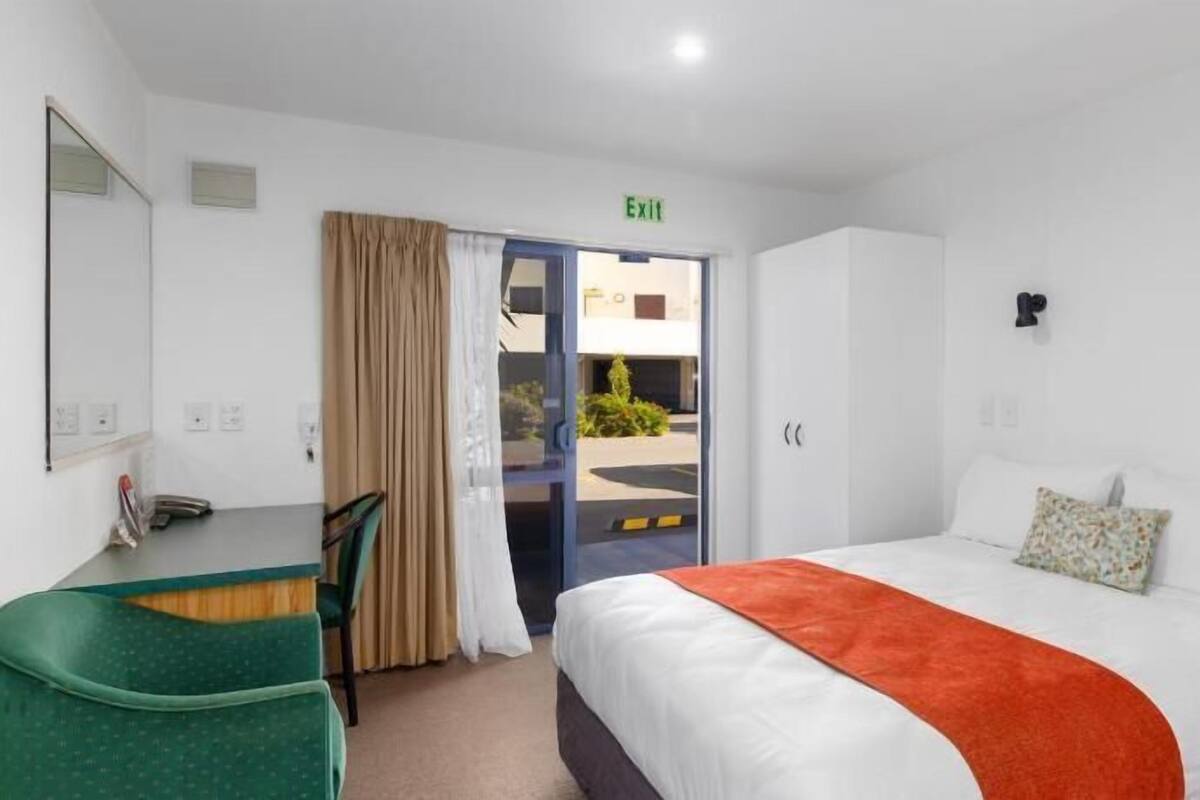 Une chambre d’hôtel avec un lit, un bureau, une chaise, un panneau indiquant la sortie et une vue sur l’extérieur.
