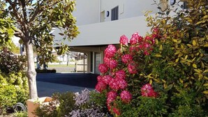 A building with a covered entrance, surrounded by lush greenery and flowering plants.