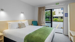 A hotel room with a bed, a chair, a small table, and an exit sign.