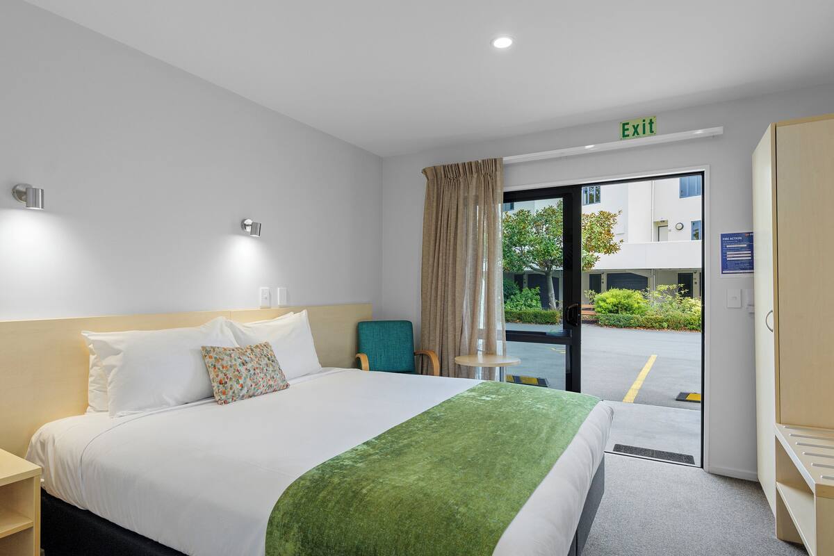 Une chambre d’hôtel avec un lit, une chaise, une petite table et un panneau indiquant la sortie.
