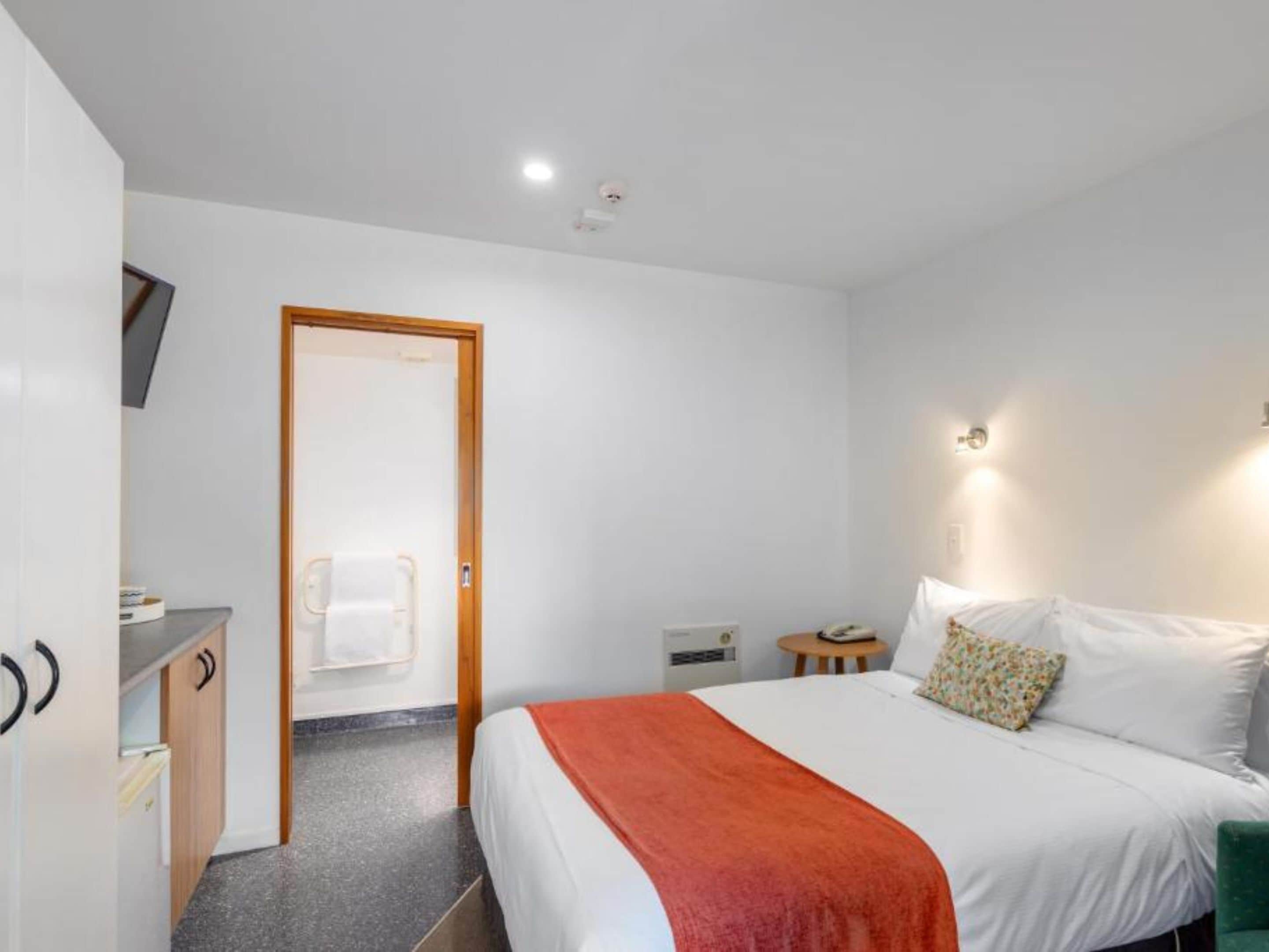 Une chambre d’hôtel comprenant un lit, un bureau, une chaise, une petite table et un téléviseur.