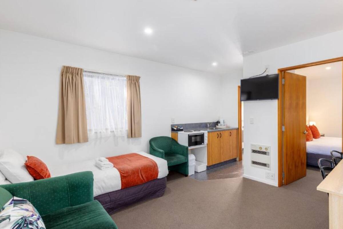 Une chambre d’hôtel de taille modeste, comprenant un canapé vert, un lit, une kitchenette et une salle de bain.