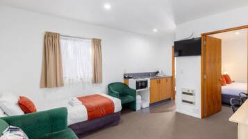 A compact hotel room with a green sofa, a bed, a kitchenette, and a bathroom.