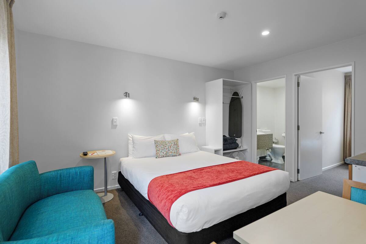 Une chambre d’hôtel avec un lit, une chaise, une petite table et une armoire.