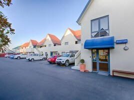 A hotel with a reception area, multiple parking spaces, and a row of similar buildings in the background.