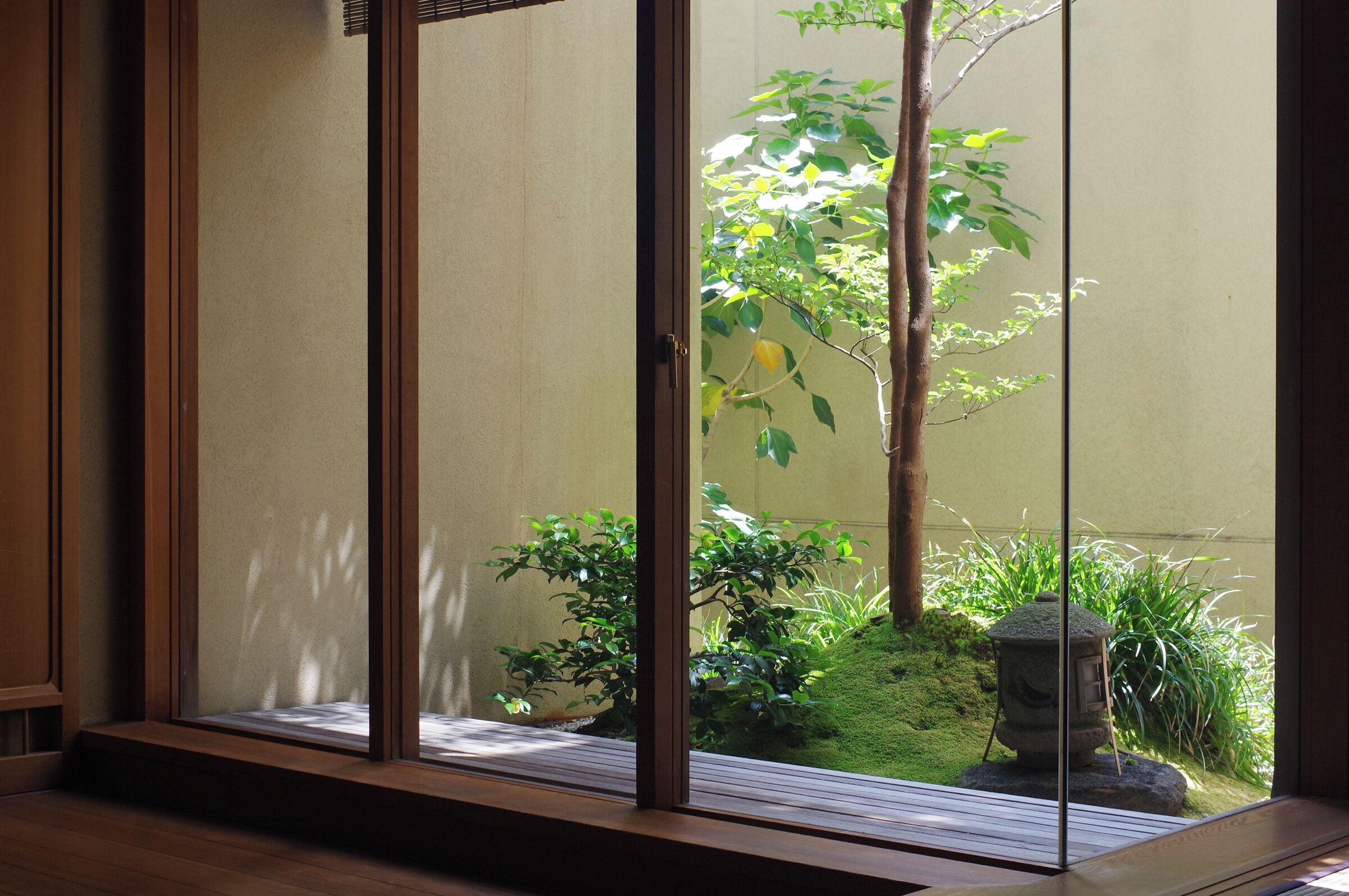A traditional Japanese room with tatami flooring, sliding shoji doors, and a view of a garden with a tree and a stone lantern.