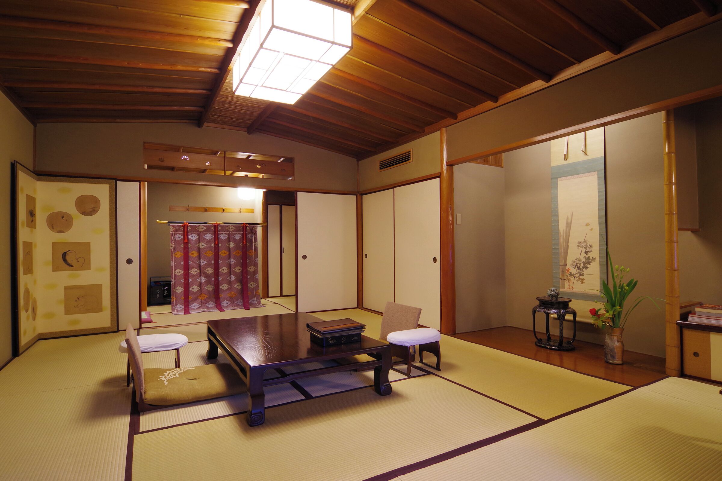 Ein traditioneller japanischer Raum mit Tatami-Bodenbelag, einem niedrigen Tisch, einem Stuhl und verschiebbaren Türen.