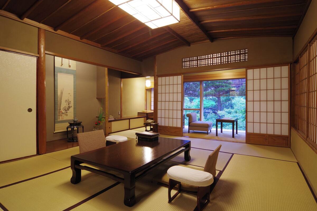 Une pièce de style japonais traditionnel, avec un sol recouvert de tatamis, une petite table en bois et une porte coulissante donnant sur un jardin.
