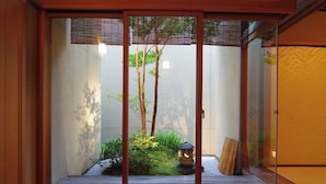 A traditional Japanese room with sliding doors, a small garden with a tree, a lantern, and a wooden bench. - Hiiragiya (Kyoto)