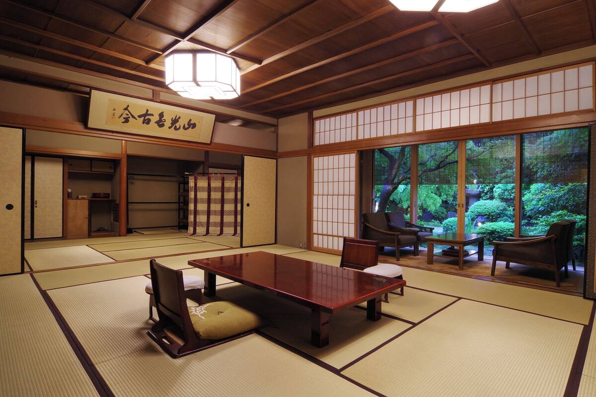 Une pièce de style japonais traditionnel, avec un sol recouvert de tatamis, une petite table en bois et des portes coulissantes donnant sur un jardin.
