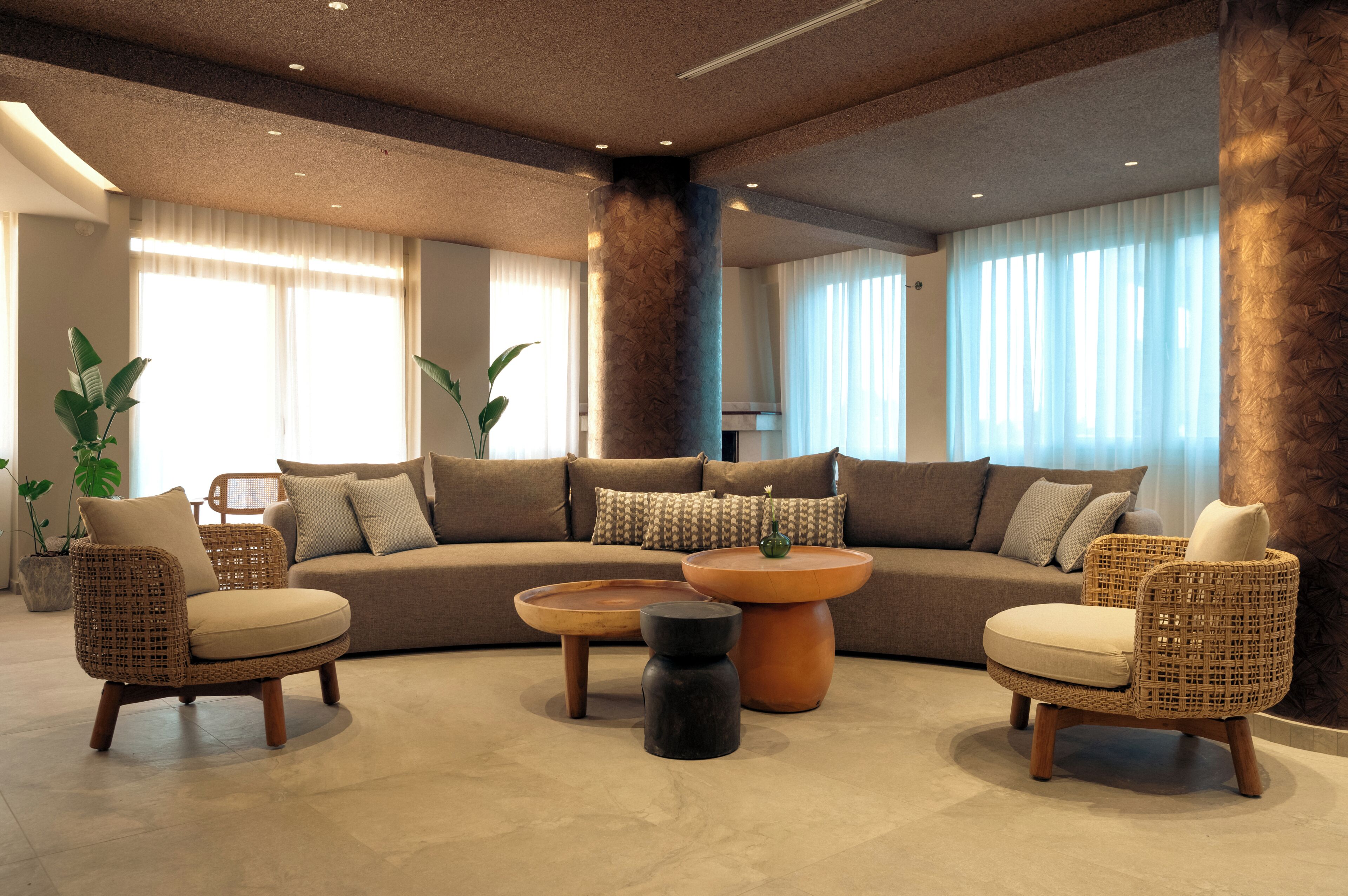 Un salon moderne comprenant un canapé d’angle, deux fauteuils en osier, une table basse ronde et une petite table d’appoint.