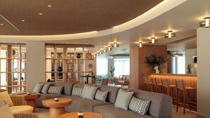 A modern lounge area with a curved sofa, round wooden tables, and a bar with high stools. - Zeus Eleva Kassandra Lagoon (Kassandra)