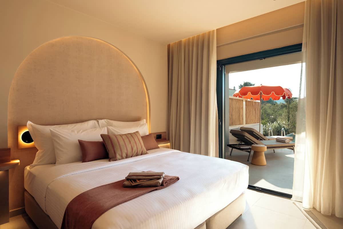 Une chambre d’hôtel avec un grand lit, une vue sur l’extérieur et un balcon agrémenté d’un parasol rouge.