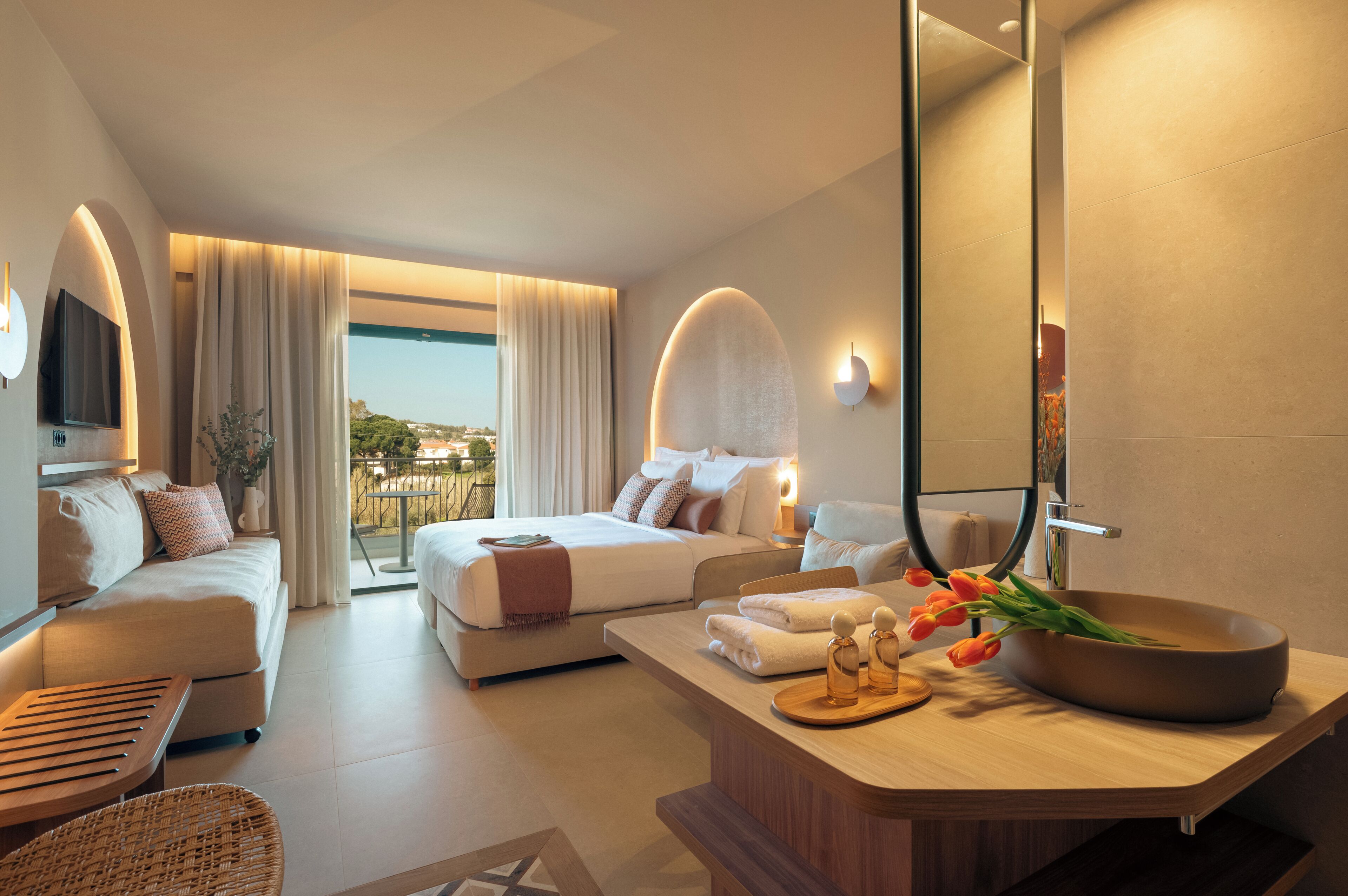 Una habitación de hotel moderna con cama, sofá y baño con un espejo grande y lavamanos.