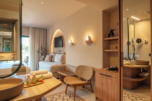 Una camera d'albergo moderna con un letto, un'area salotto, un armadietto in legno, uno specchio grande e un bagno con lavandino e doccia.