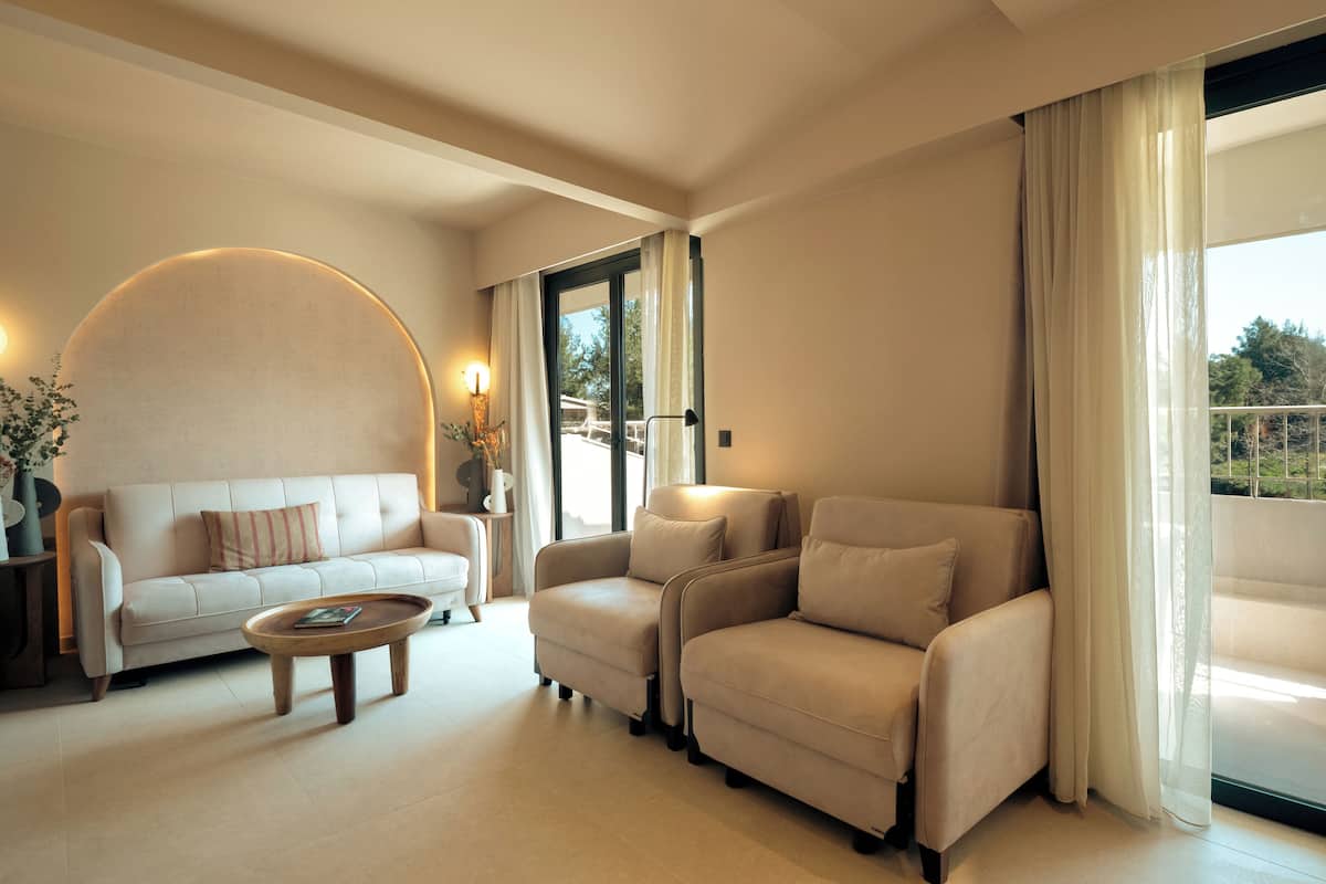Un salon moderne avec un canapé, des fauteuils, une table basse et une grande fenêtre agrémentée de rideaux.