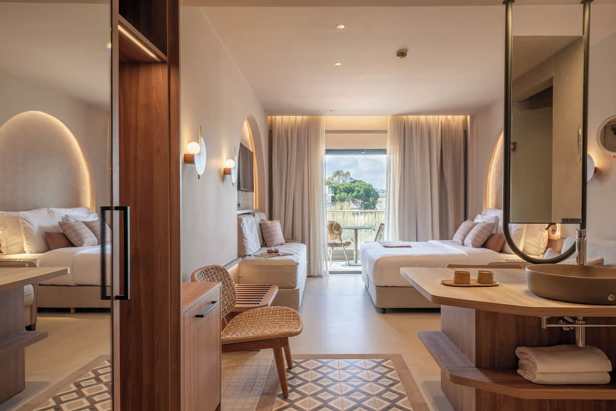Une chambre d’hôtel comprenant un lit, un bureau, une chaise, une salle de bain avec un lavabo et un miroir, et donnant sur l’extérieur.